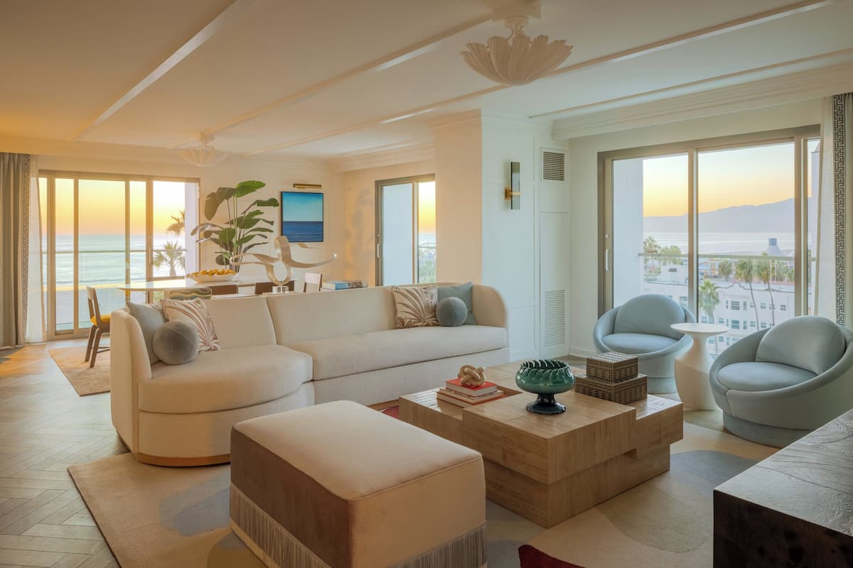 A modern living room with a sofa, armchairs, a coffee table, and a view of the ocean at sunset.