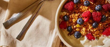Deux bols de céréales avec des fruits rouges et du granola, une cuillère, une serviette et une tasse de café sur une table.