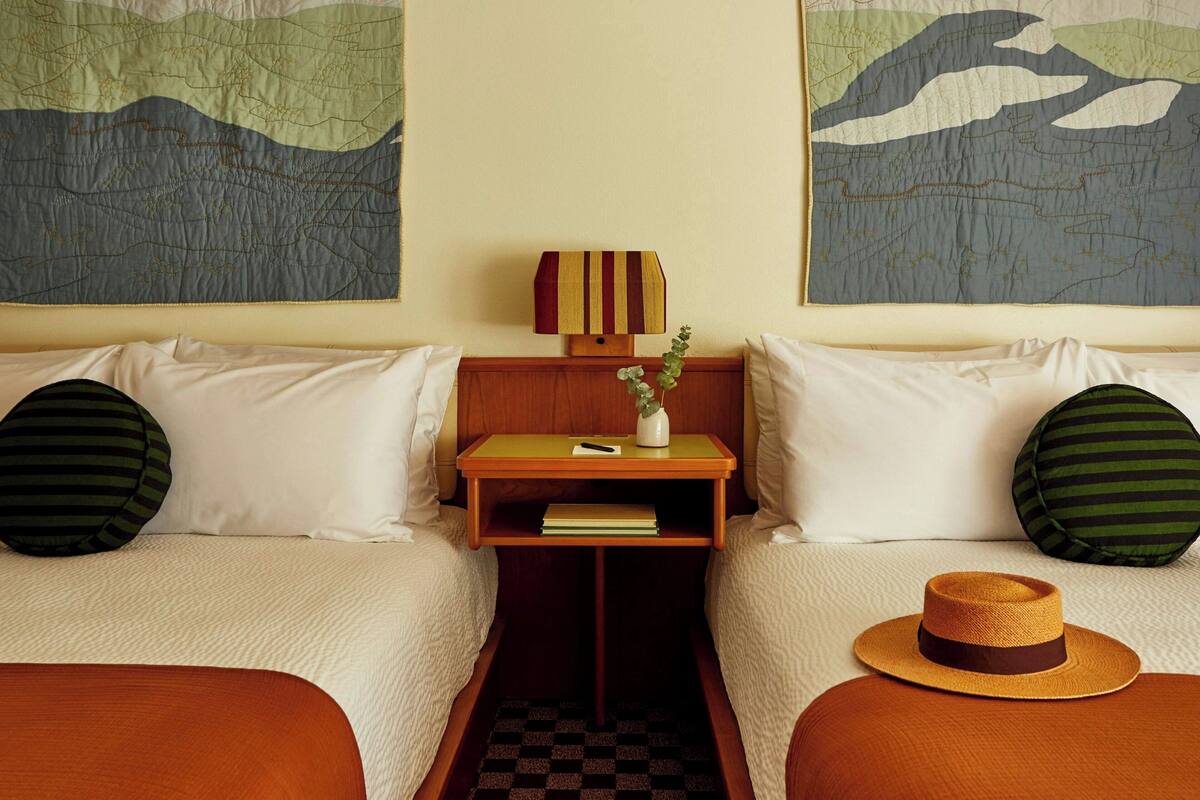 Une chambre d’hôtel avec deux lits, une table de chevet, une lampe et des œuvres d’art accrochées aux murs.
