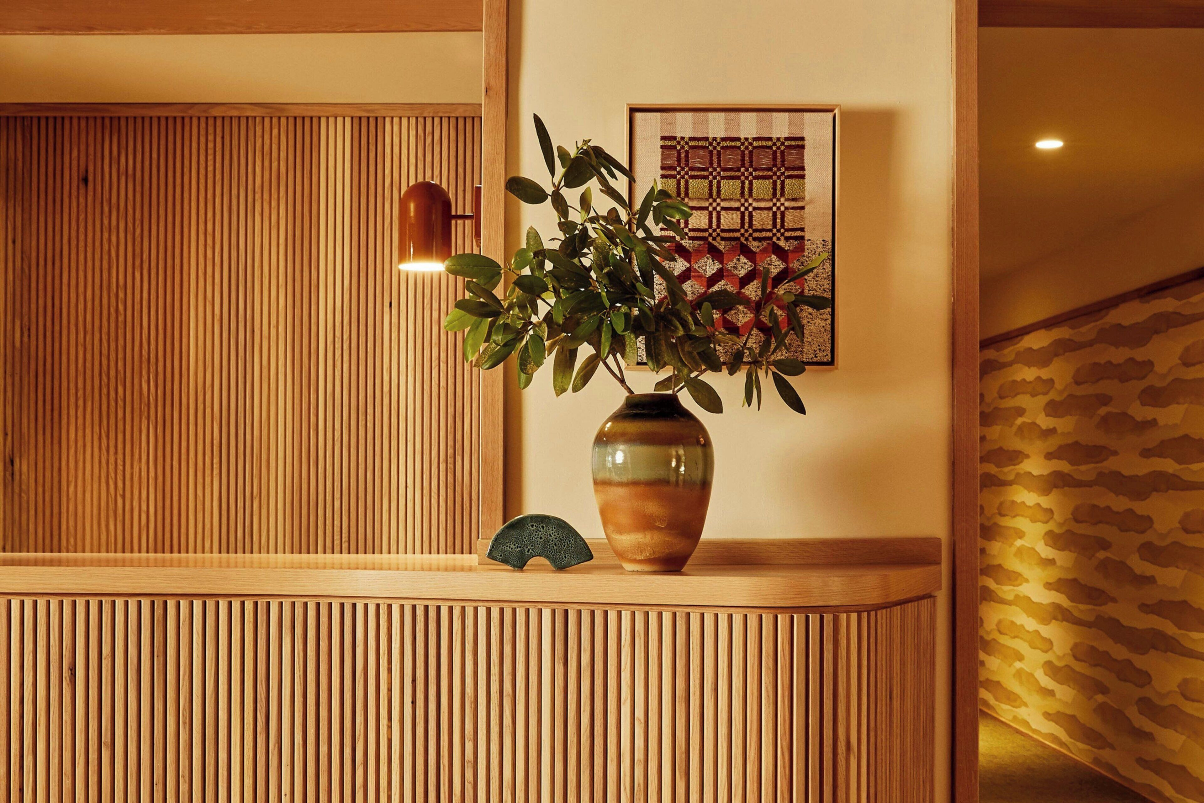 Un mostrador de recepción de madera con un florero de hojas verdes y un colcha enmarcada.