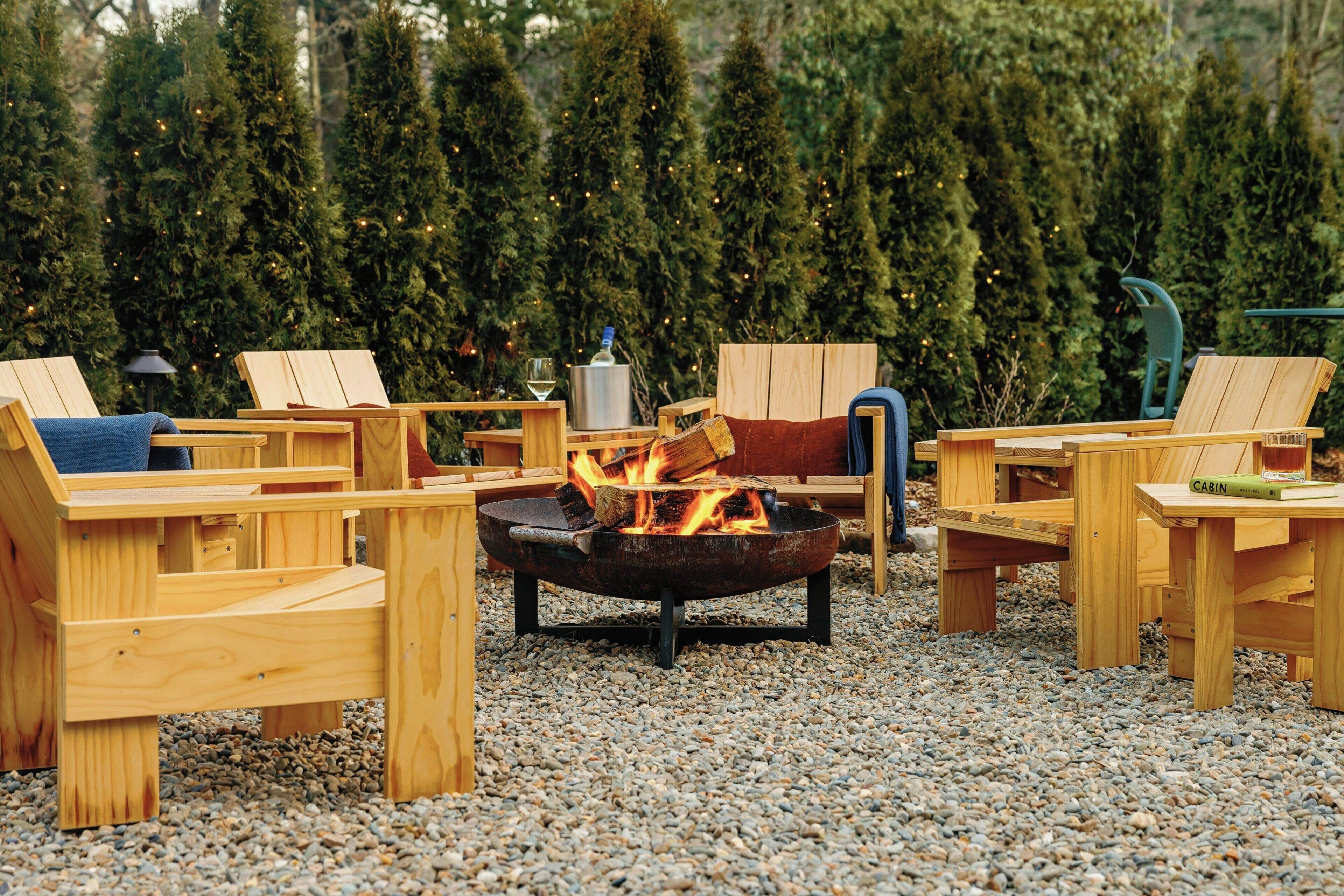 A wooden outdoor seating area with a fire pit in the center, surrounded by chairs and tables.