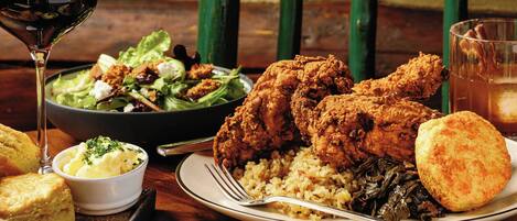 A plate of fried chicken, rice, greens, and biscuits on a wooden table with a glass of red wine.