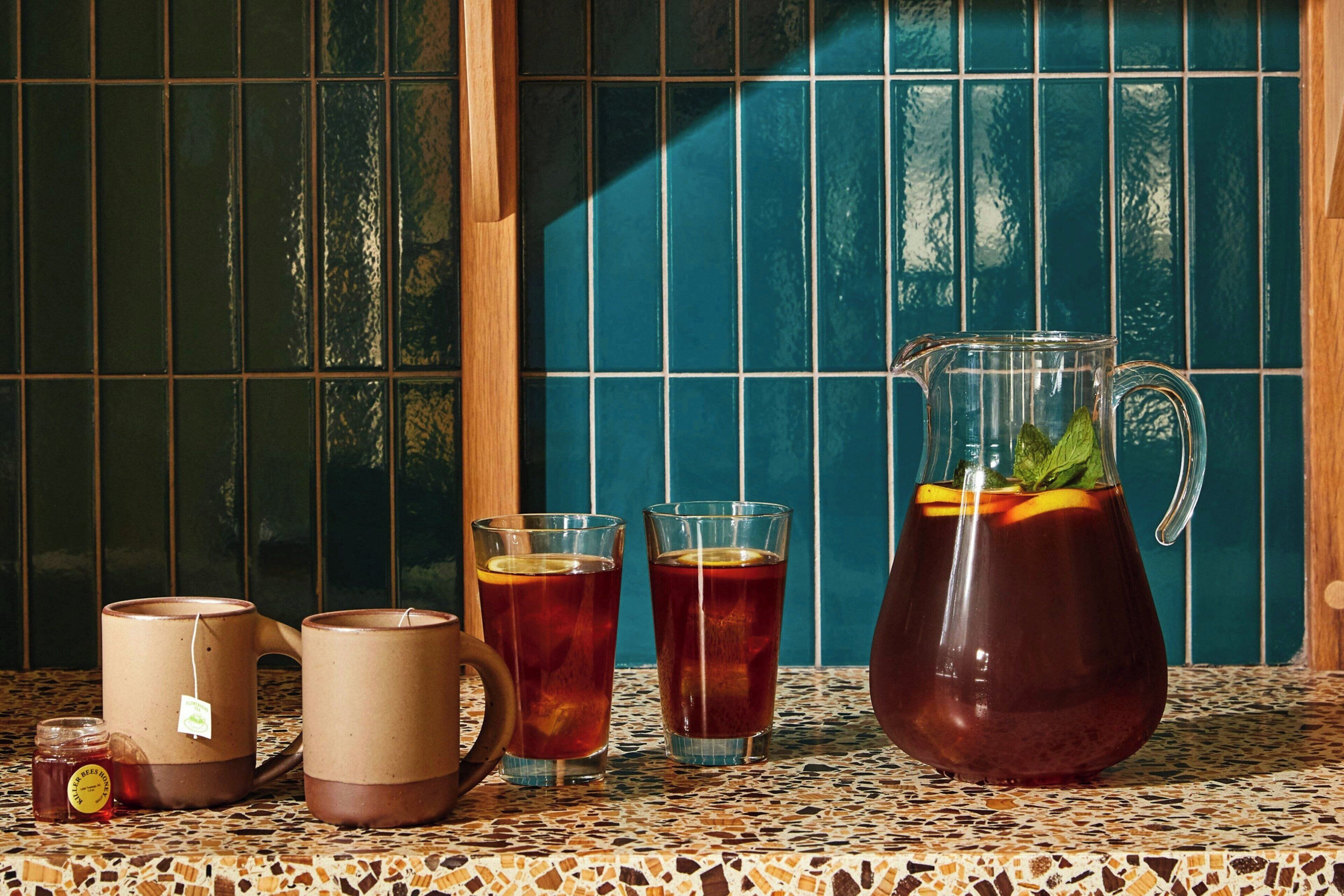 En köksbänk klädd med kakelplattor, med en kanna iskallt te, två glas och en mugg på.