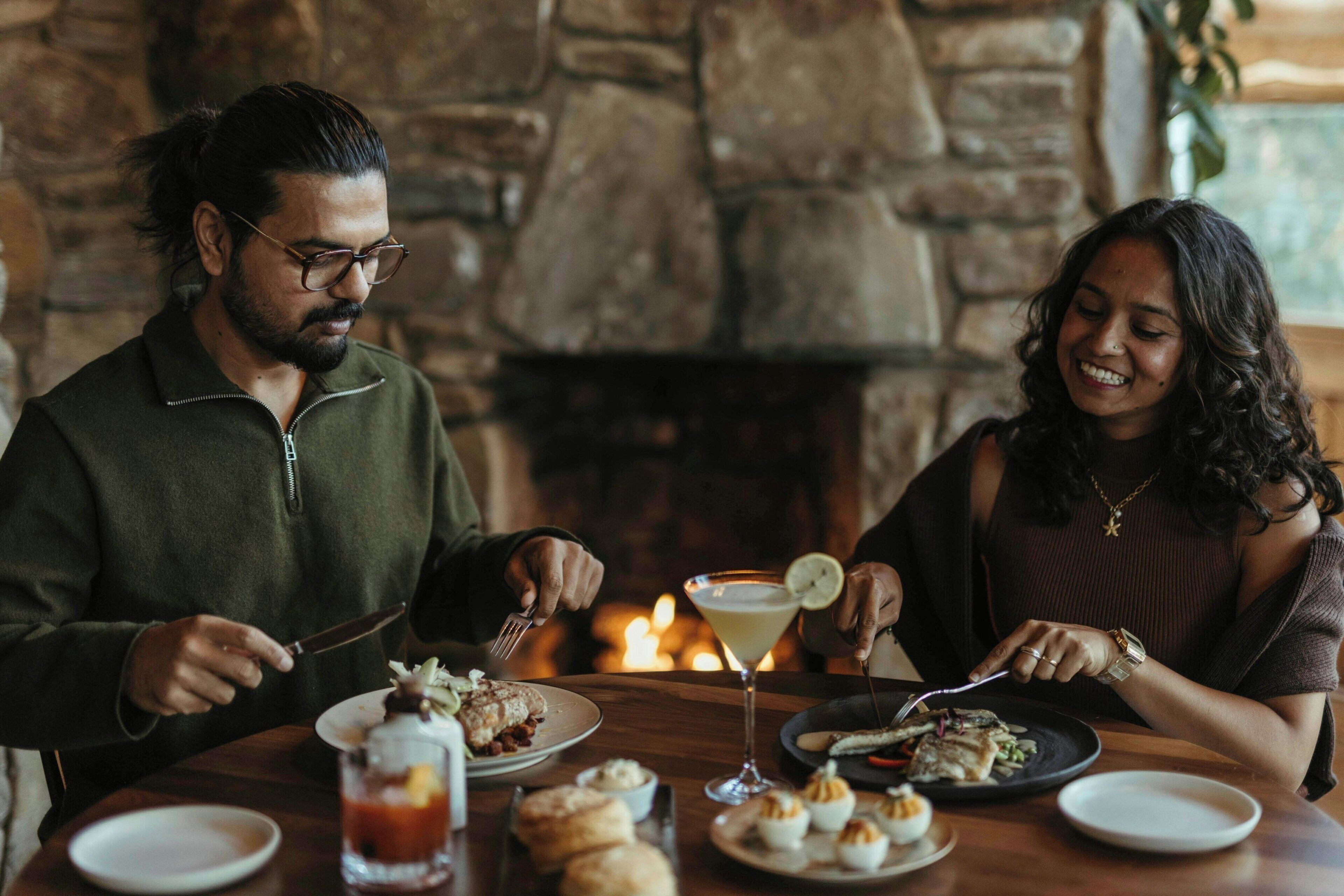 A couple dining at a table with a stone fireplace in the background.