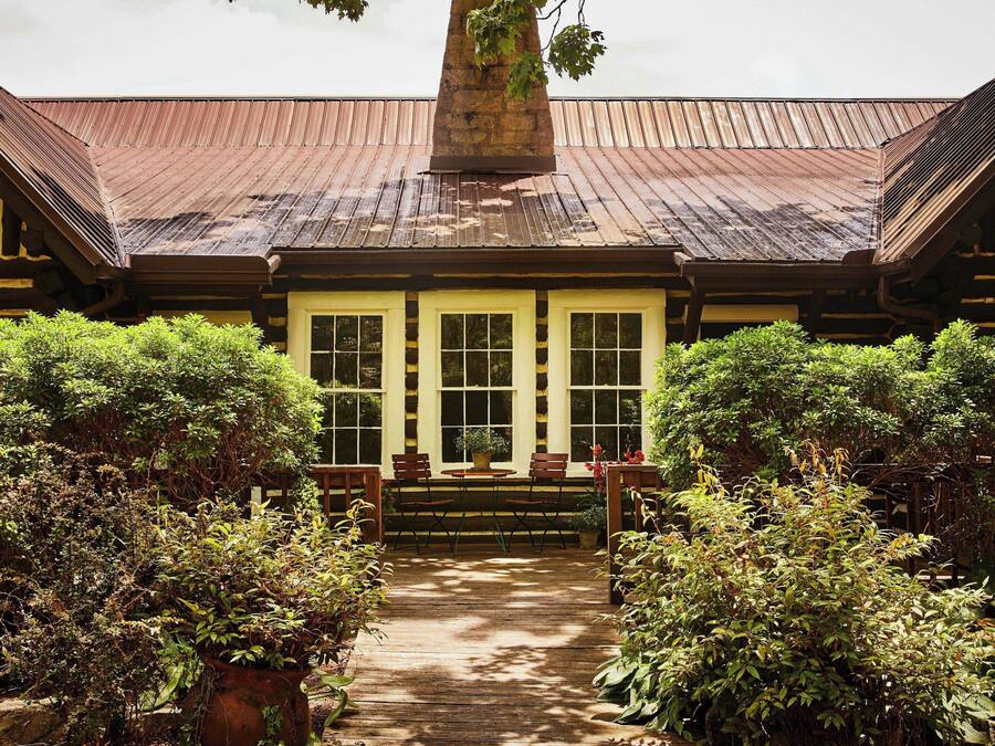 A covered outdoor area with a wooden deck, a central seating area with chairs, and a large window with multiple panes.