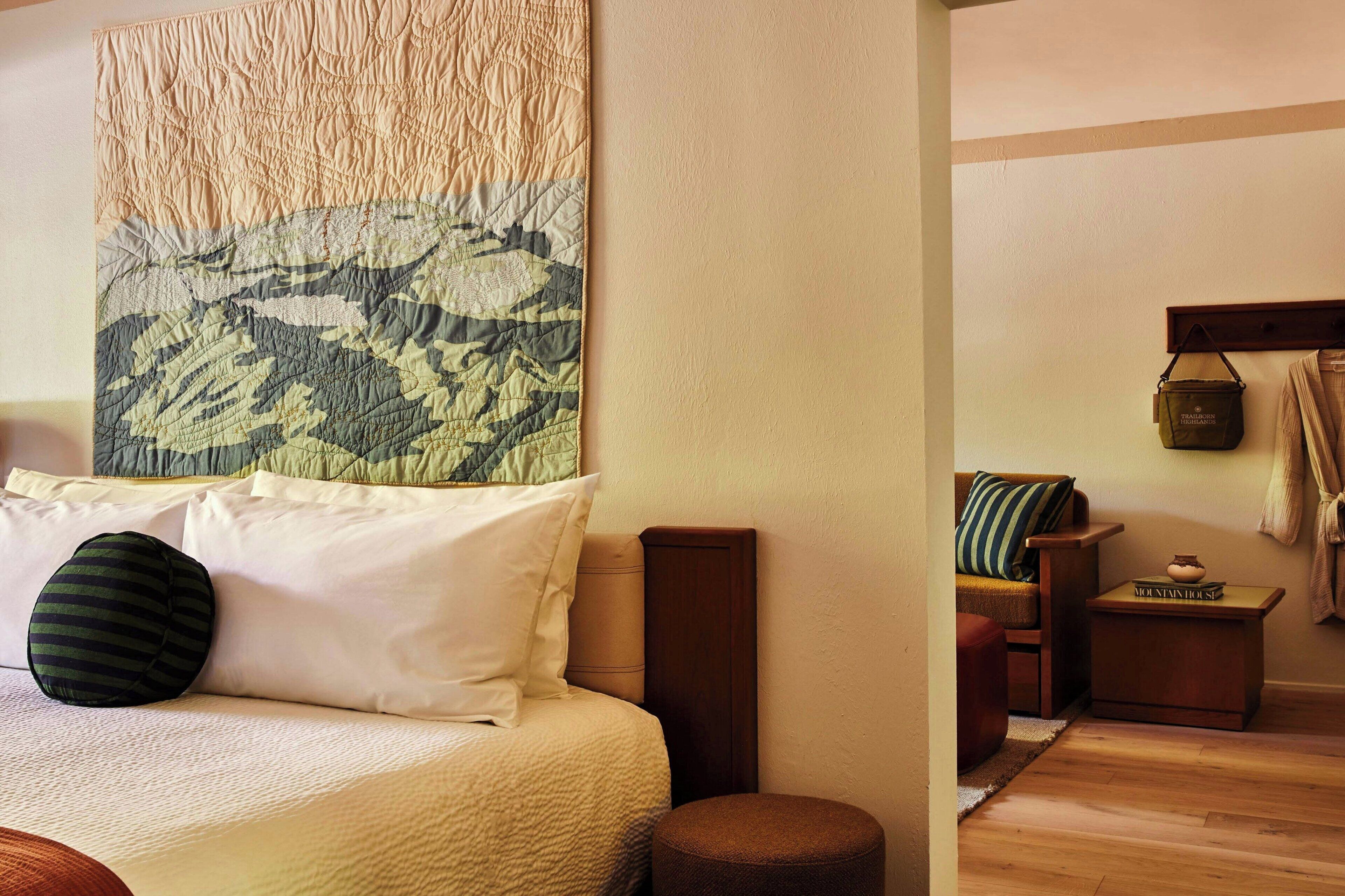 A neatly arranged bedroom with a bed, pillows, a bedside table, and a hanging tapestry.