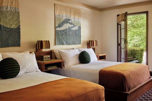 A hotel room with two beds, a large window, and artwork on the walls.