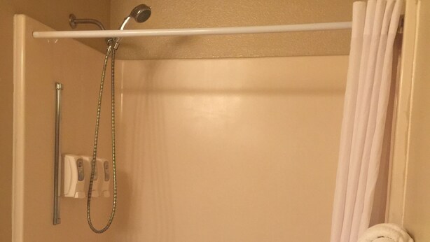A standard hotel bathroom with a bathtub, a shower, grab bars, a towel rack, and a curtain.
