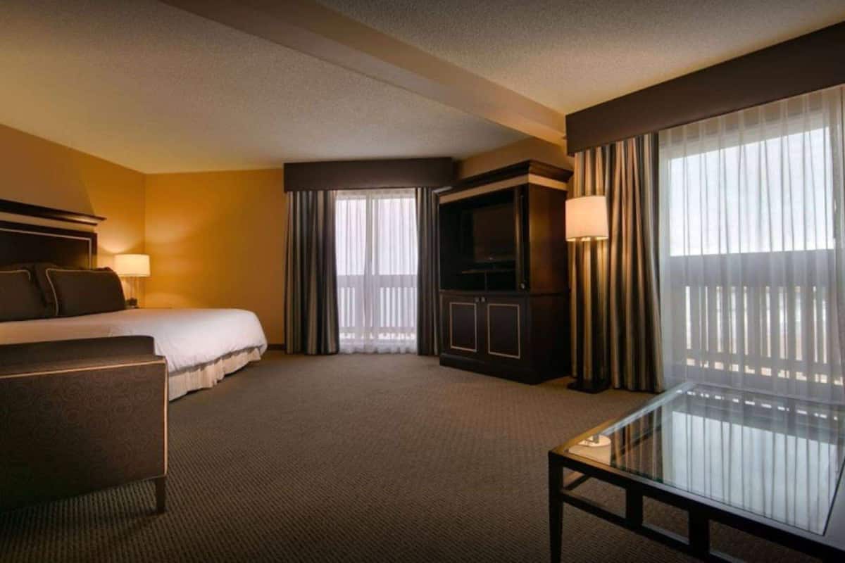 A hotel room with a bed, a desk, a TV, and a large window with curtains.