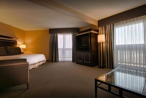 A hotel room with a bed, a desk, a TV, and a large window with curtains.