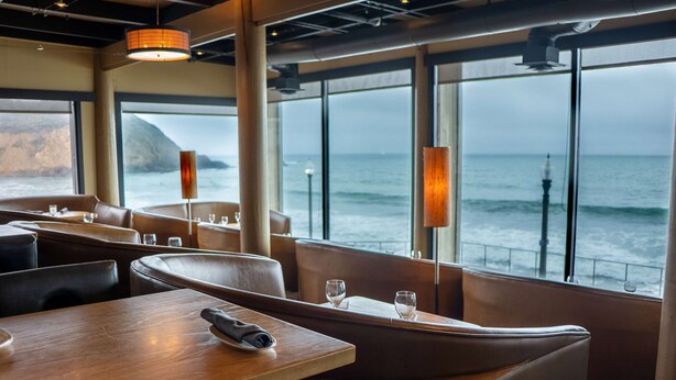 A restaurant with tables and booths, large windows with ocean views, and a high ceiling with exposed beams. - Pacifica Lighthouse Hotel Trademark Collection by Wyndham (Pacifica)