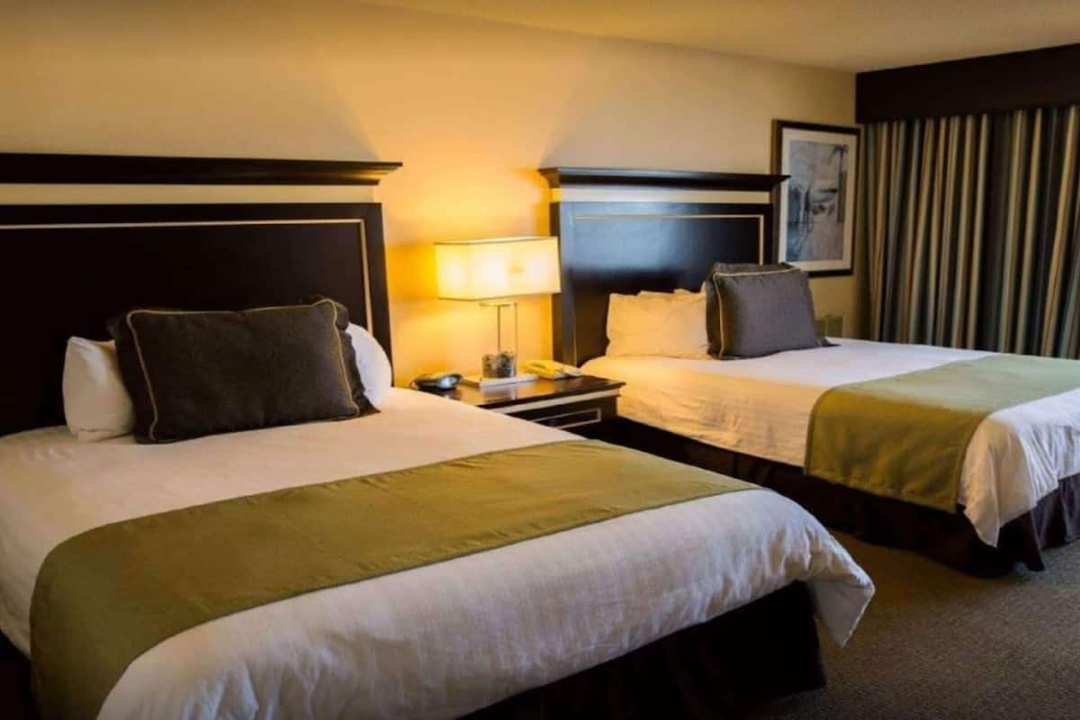 A hotel room with two beds, each with a headboard, bedside tables, lamps, and a framed picture on the wall.