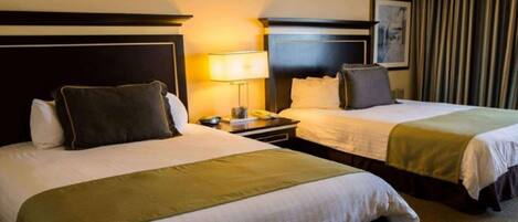 A hotel room with two beds, each with a headboard, bedside tables, lamps, and a framed picture on the wall.