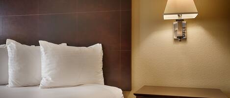 Une chambre d’hôtel avec un lit, deux oreillers, une table de chevet et une lampe fixée au mur.