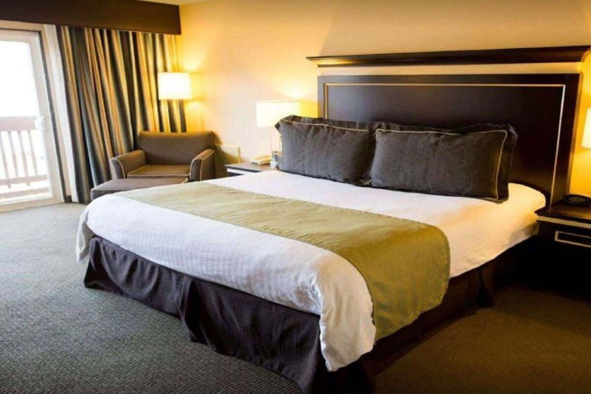 A hotel room with a large bed, a chair, a nightstand, and a lamp.