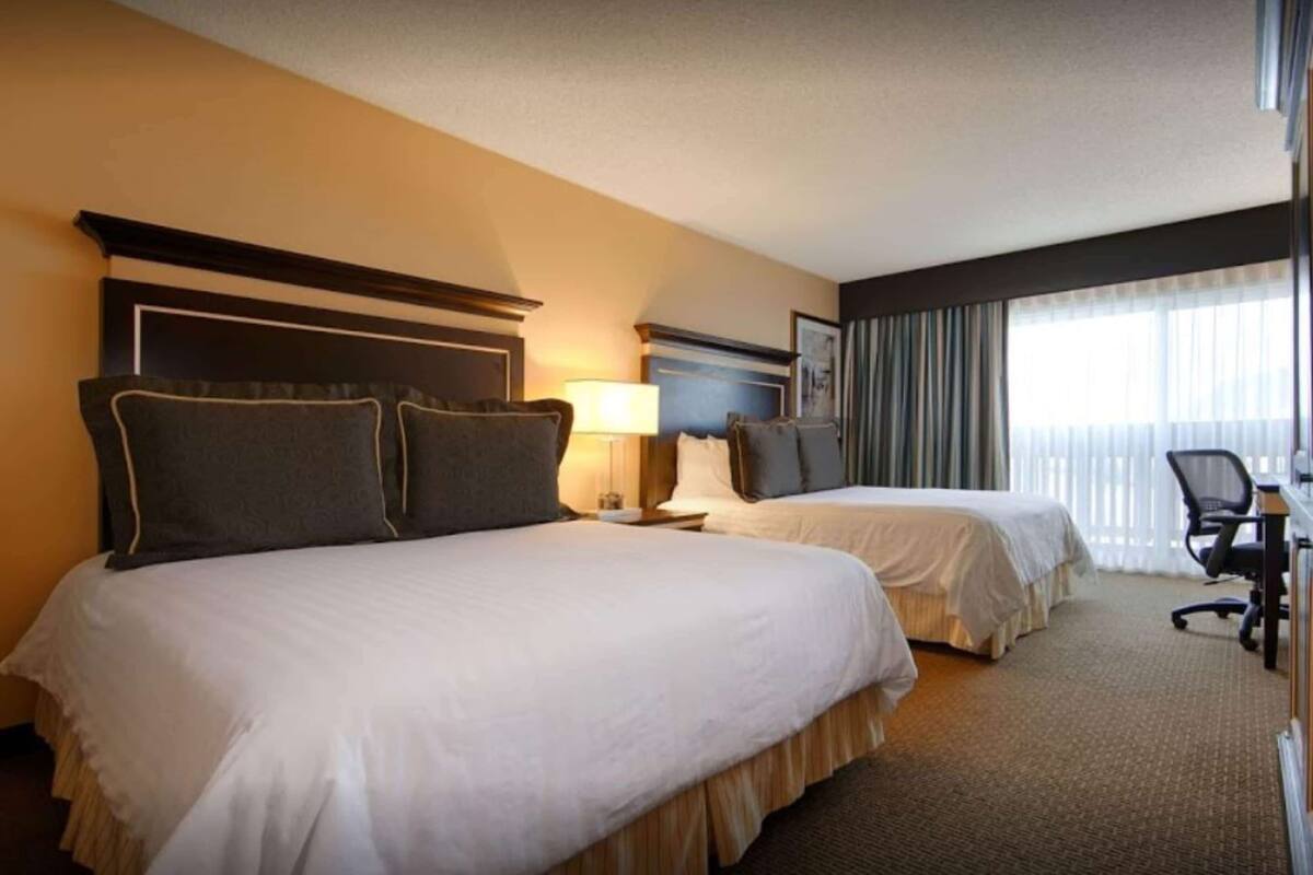 A hotel room with two beds, a desk, and a chair.