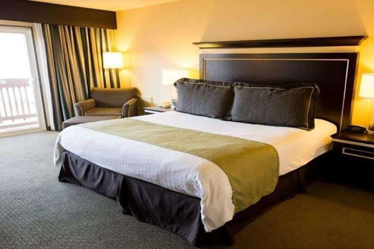 A hotel room with a large bed, two bedside tables, a chair, and a view of the outdoors.