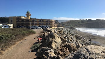 A coastal hotel with a rocky walkway leading to the beach, a parking area, and a view of the ocean.