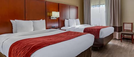 A hotel room with two beds, a wooden headboard, a nightstand, a chair, and a window with curtains.