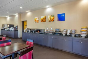 A hotel breakfast area with a buffet, seating, and a wall with fruit-themed artwork. - Comfort Inn Fort Mill Amusement Park at Carowinds Blvd (Fort Mill)