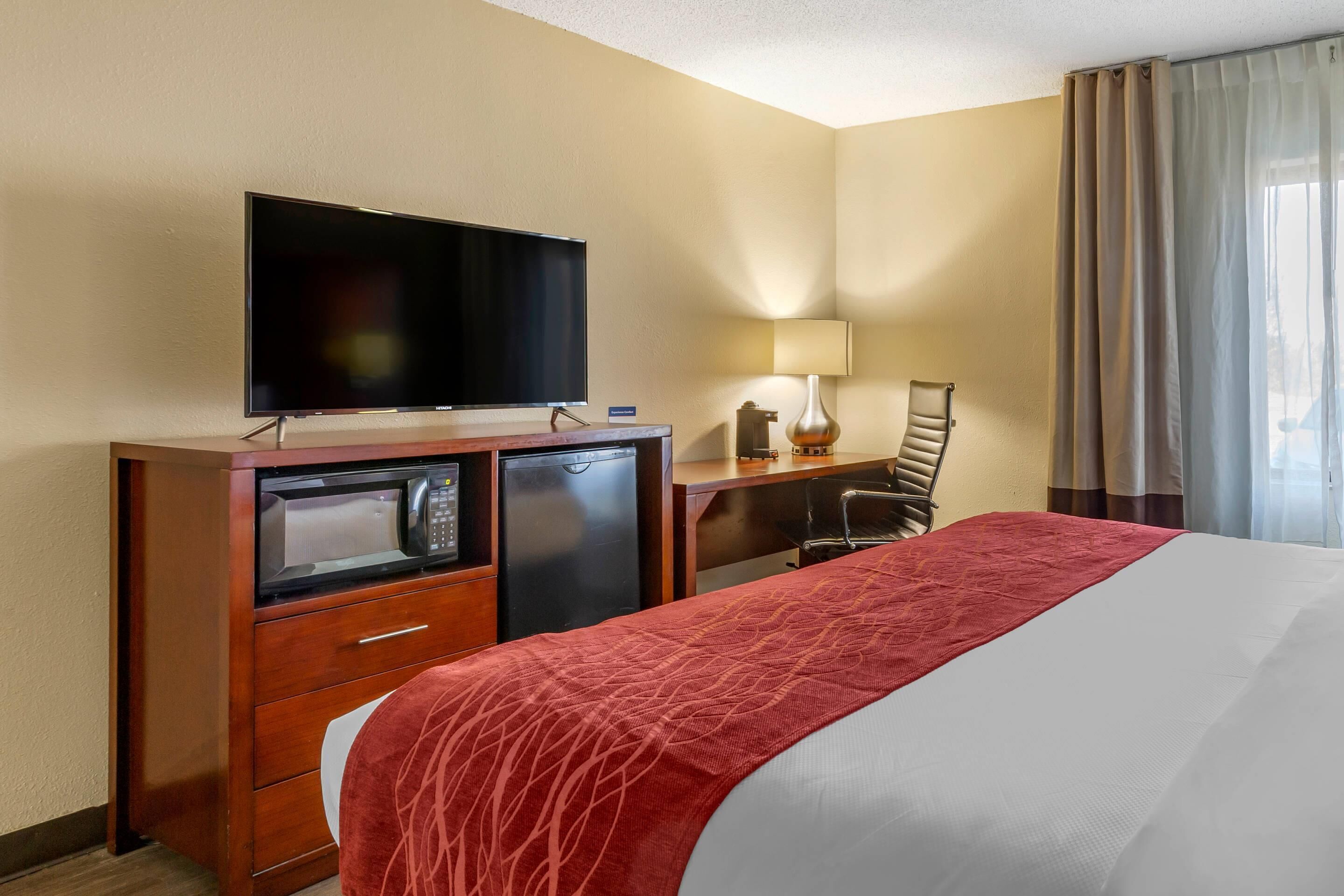 A hotel room with a bed, a TV, a desk with a lamp, a chair, and a microwave.