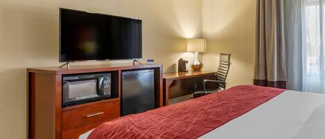 A hotel room with a bed, a TV, a desk with a lamp, a chair, and a microwave.