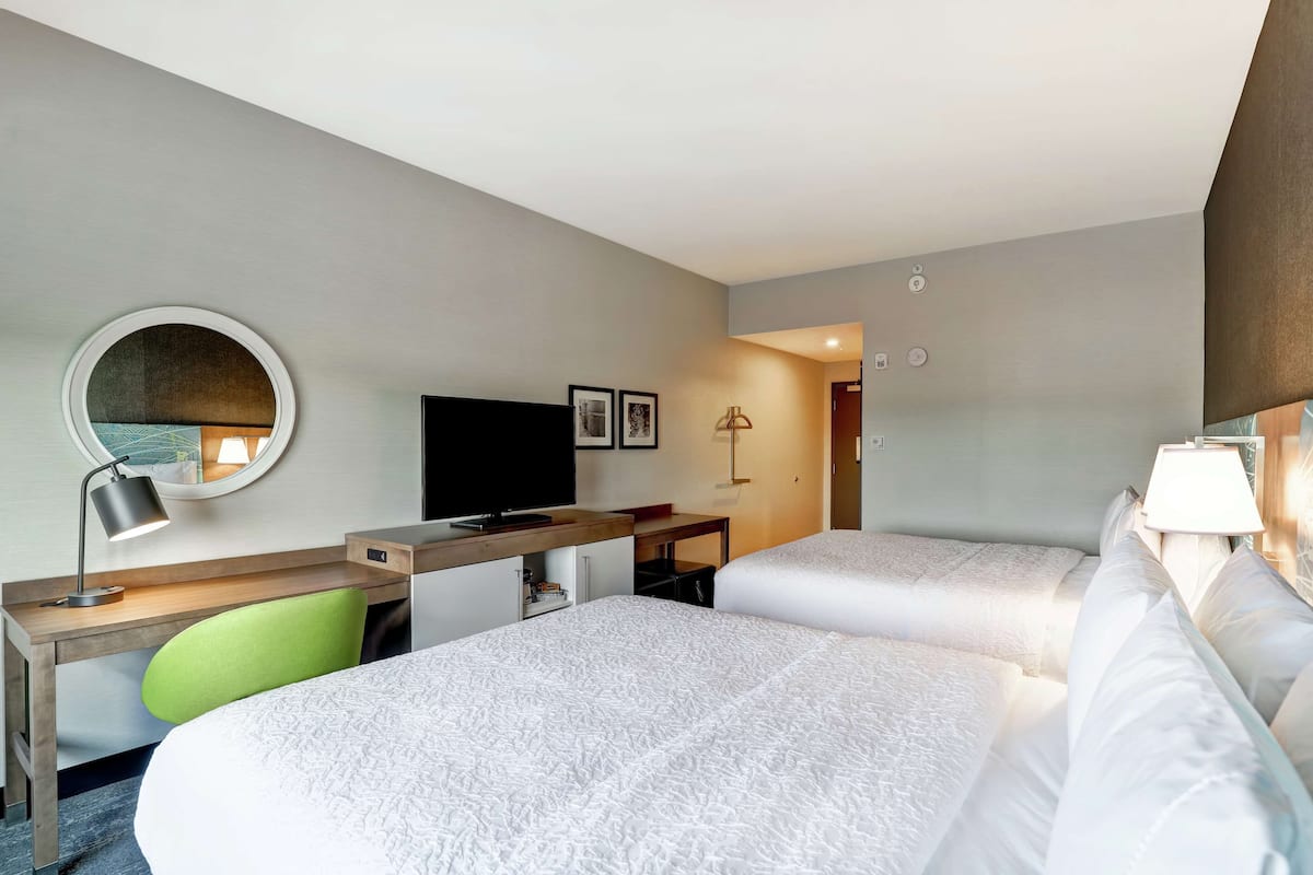 Una habitación de hotel con dos camas, un escritorio con computadora, un televisor y un espejo.