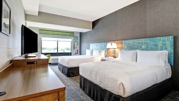 A hotel room with two beds, a desk, a TV, and a window with a view.