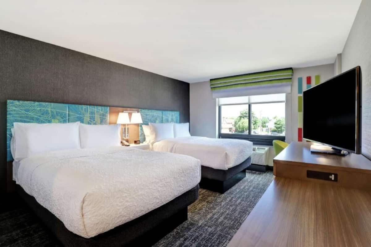Habitación de hotel con dos camas, televisión, lámpara y ventana con vistas.