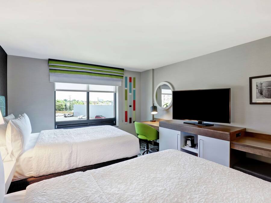 A hotel room with two beds, a desk, a television, and a window with a view of the outside.