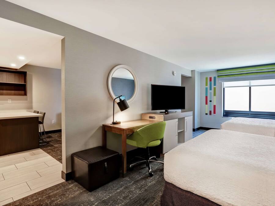 Quarto de hotel com escrivaninha, cadeira, televisão e duas camas.