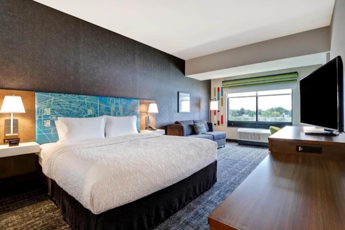 Habitación de hotel con una cama grande, un escritorio, un televisor y vistas al exterior.