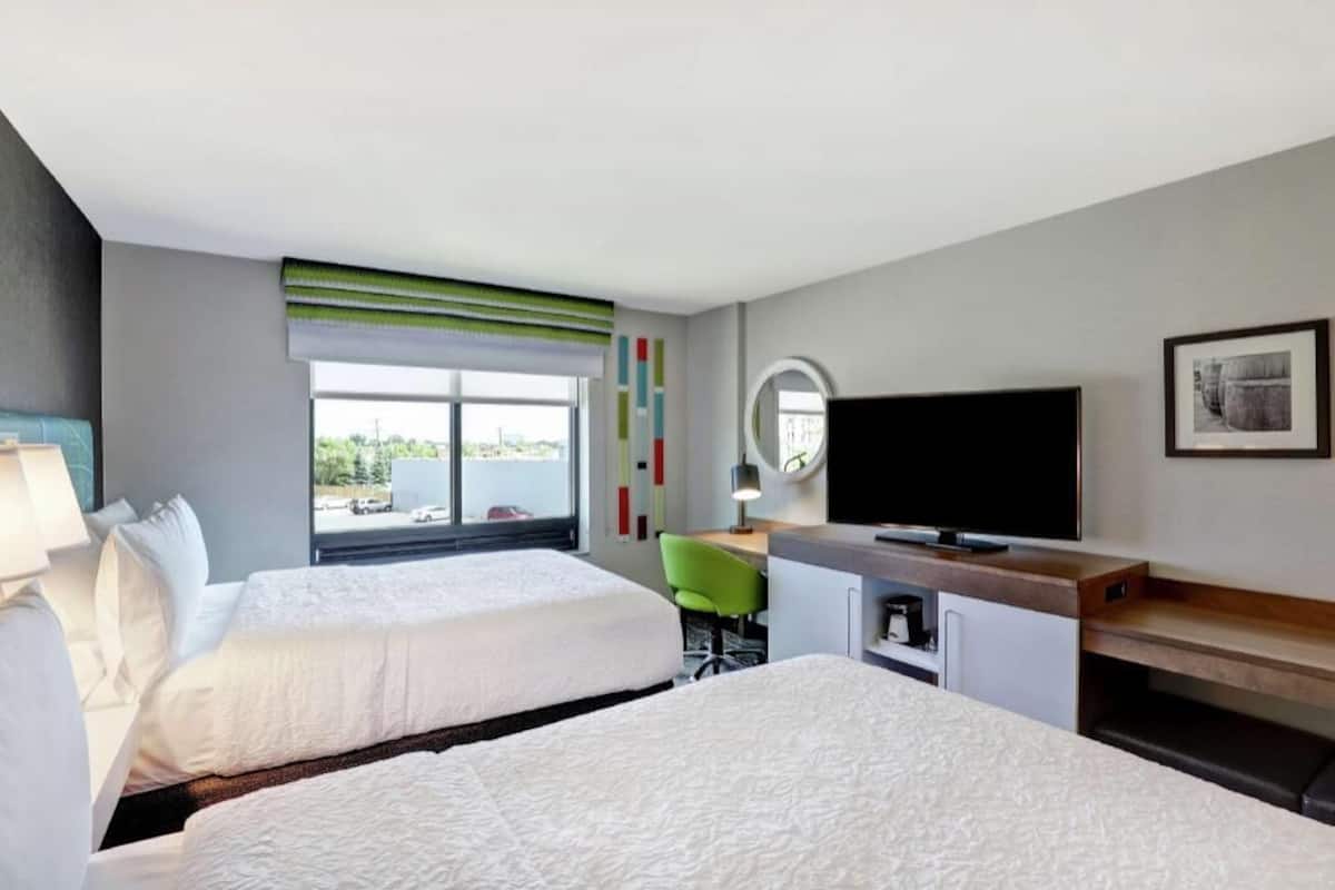 Habitación de hotel con dos camas, un escritorio, televisor y ventana con vistas.
