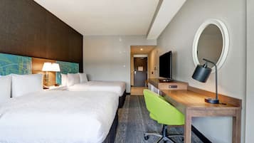Una habitación de hotel con dos camas, un escritorio con silla, un televisor, un espejo y una lámpara.