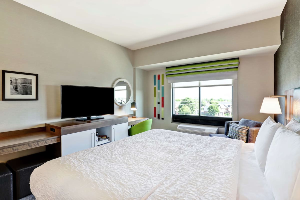 Habitación de hotel con una cama grande, un escritorio con televisión de pantalla plana, una silla, una ventana con vistas y una mesita de noche con lámpara.