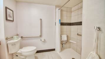 Un baño con inodoro, barras de apoyo, zona de ducha y un perchero para toallas.
