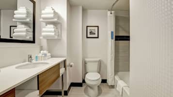 Un baño moderno con un lavamanos, espejo y retrete blancos. Hay toallas en estantes y un cuadro enmarcado en la pared.