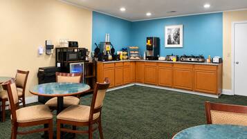 A hotel room with a kitchenette, a dining area with a round table and chairs, and a blue accent wall.