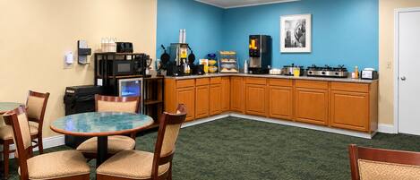 A hotel room with a kitchenette, a dining area with a round table and chairs, and a blue accent wall.