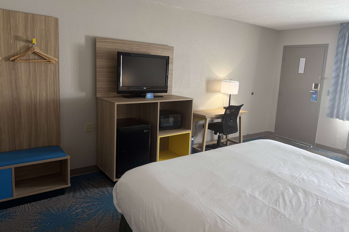 Una habitación de hotel con una cama, un escritorio con computadora, televisión y armario.