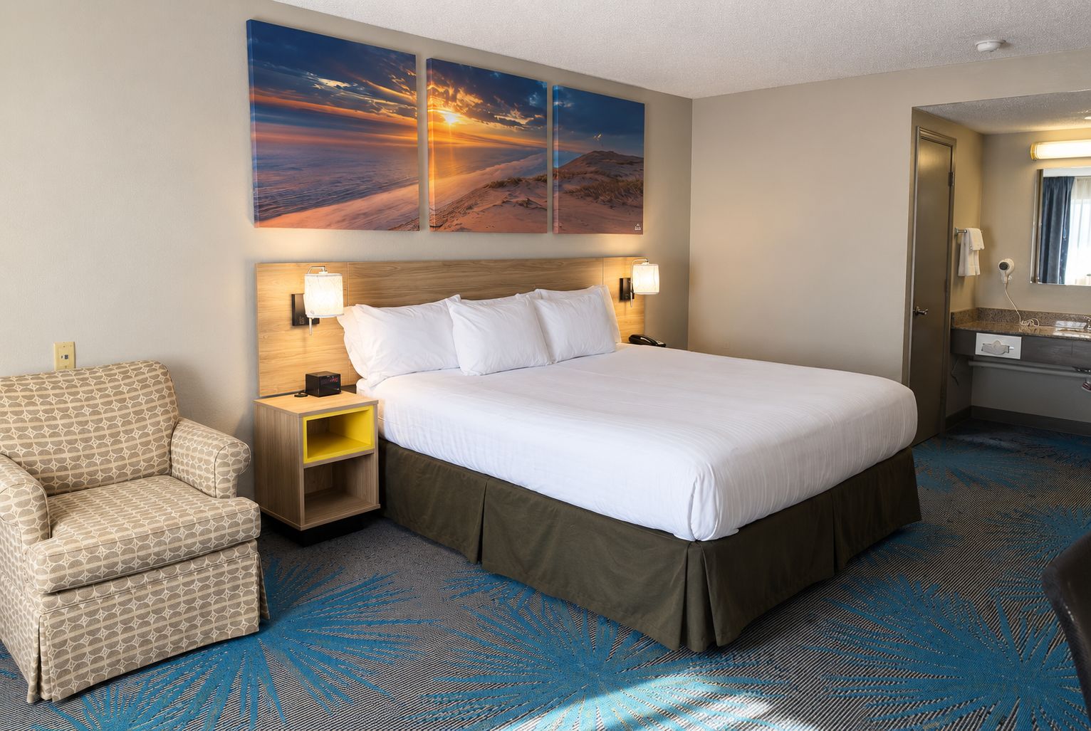 A hotel room with a large bed, a chair, a nightstand, and a wall-mounted lamp.
