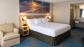 A hotel room with a large bed, a chair, a nightstand, and a wall-mounted lamp.