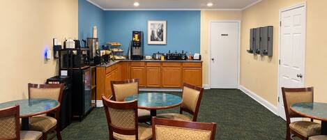 A hotel room with a dining area, kitchenette, and a door leading to a hallway.