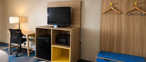 Habitación de hotel con cama, escritorio con computadora, televisor, microondas y armario con perchas.