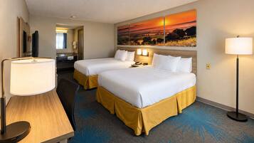 A hotel room with two beds, a desk, a lamp, a painting, and a carpet.