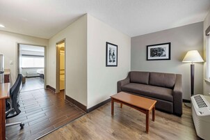 A modern living room with a sofa, a coffee table, and a lamp. There are two framed pictures on the wall and a window with blinds.