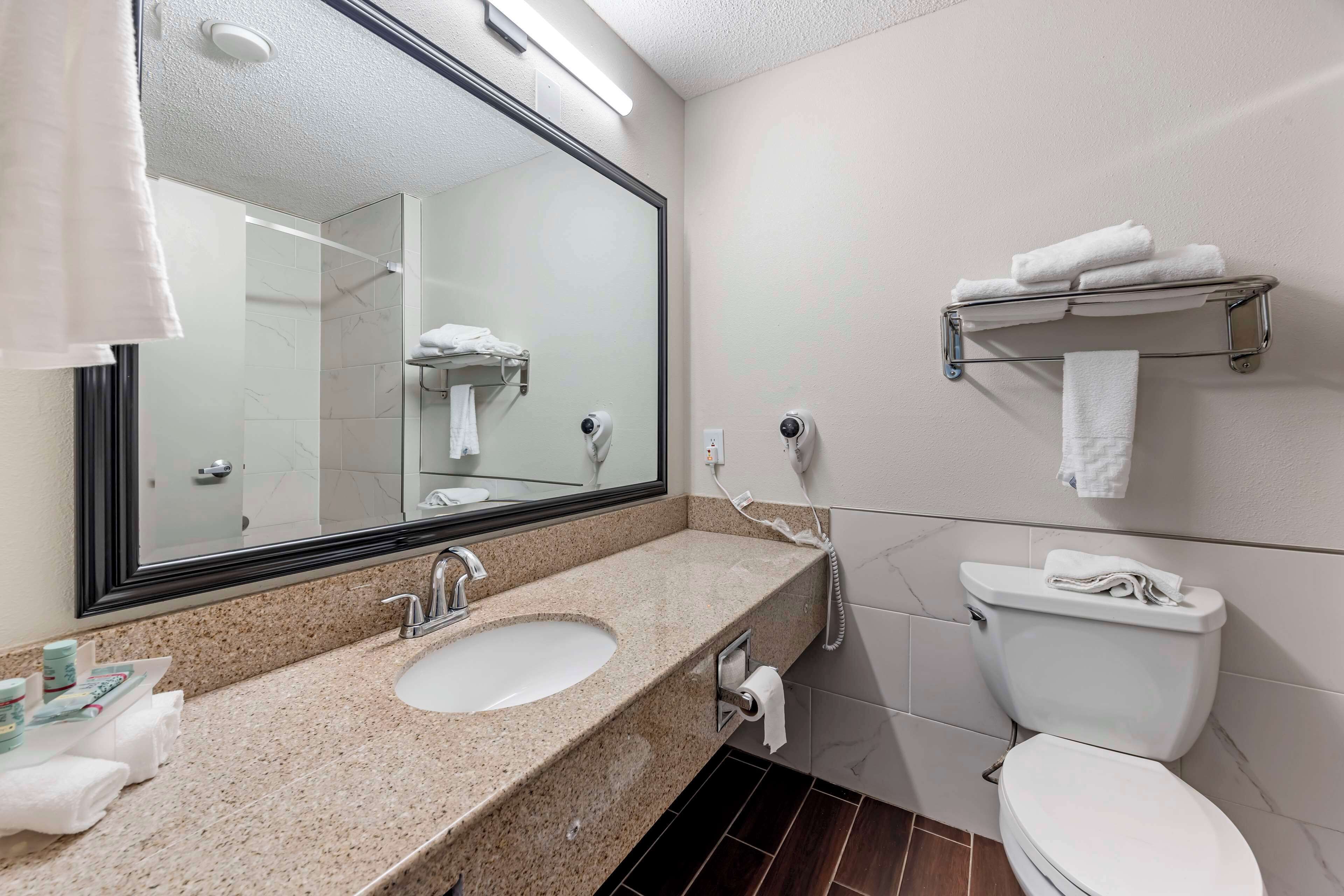 Un baño con lavabo de encimera de granito, un espejo grande, inodoro y toallero.