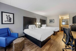A hotel room with a large bed, a desk, a chair, a sofa, and two framed pictures on the wall.