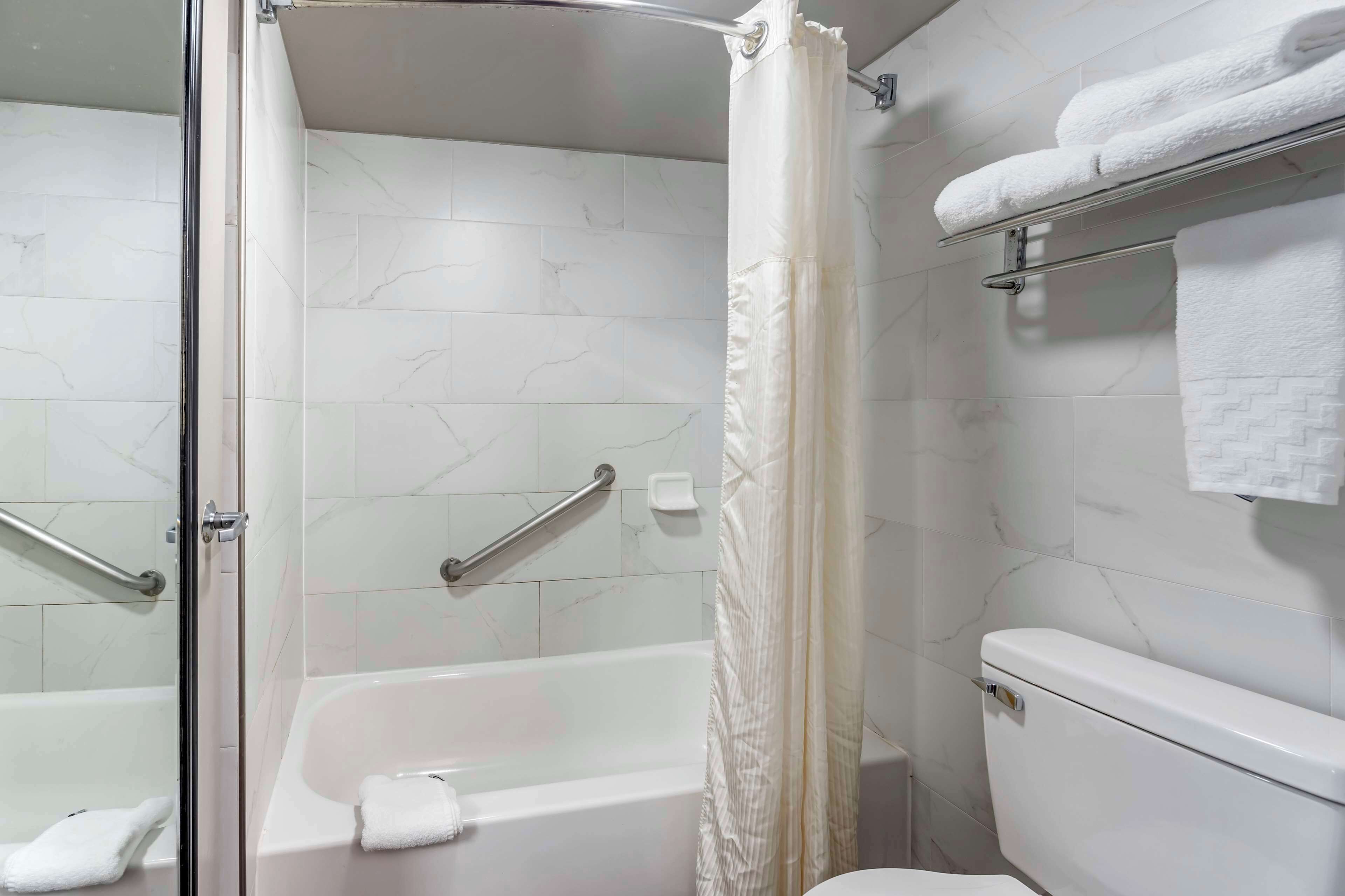 Un baño con ducha de mampara de vidrio, bañera, inodoro y toallero con toallas.