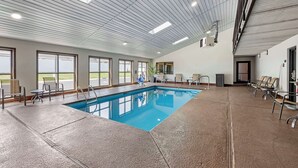An indoor swimming pool with a view of the outdoors, ceiling lights, and seating areas.